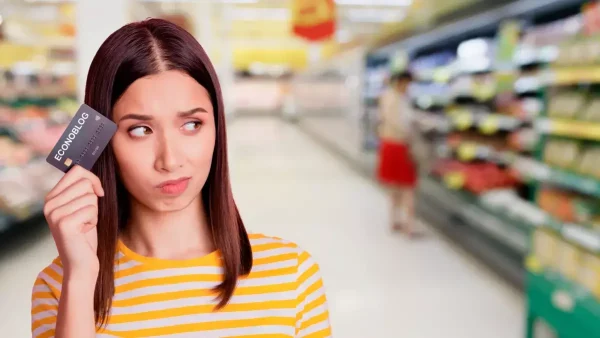 Mujer preocupada en supermercado con tarjeta de débito en la mano