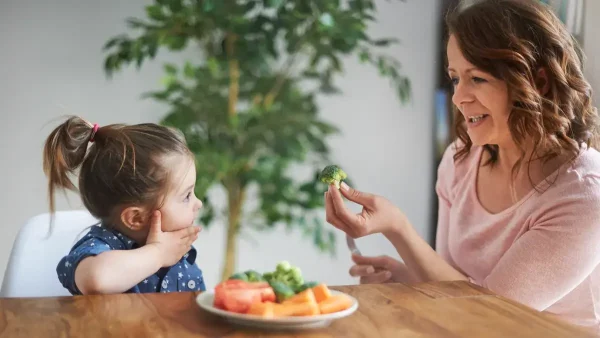Madre comiendo verduras con su hija